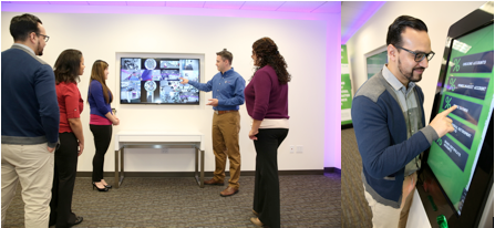 Five people standing looking at a screen that appears to be a presentation. One man presenting
